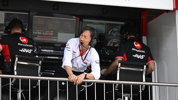 A man with a headset looks over a Formula One race area from a control box